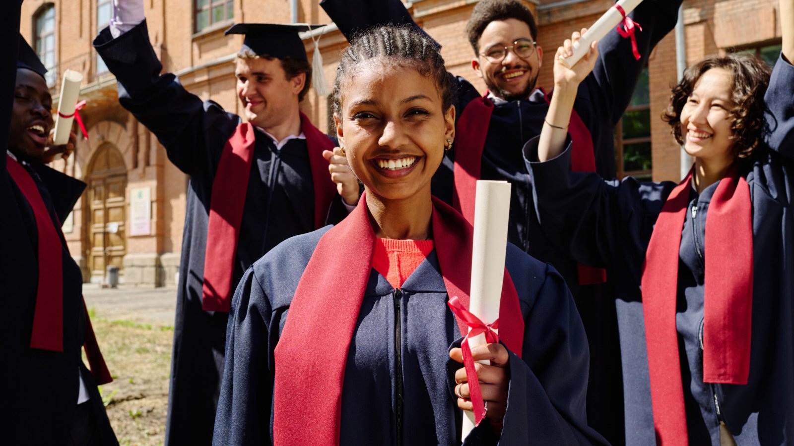 Portrait of happy graduated student with diploma smiling at camera with her friends celebrating graduation in background